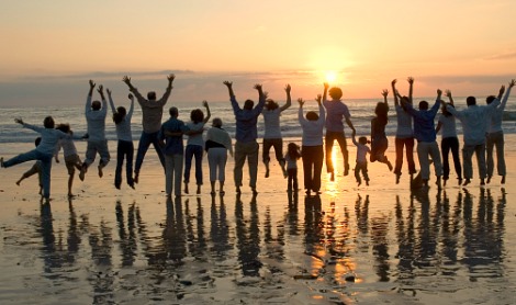 Large group of family members of varying ages jumping at a beach while the sun sets