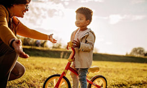Little boy on his bike in a field is encouraged by his mom