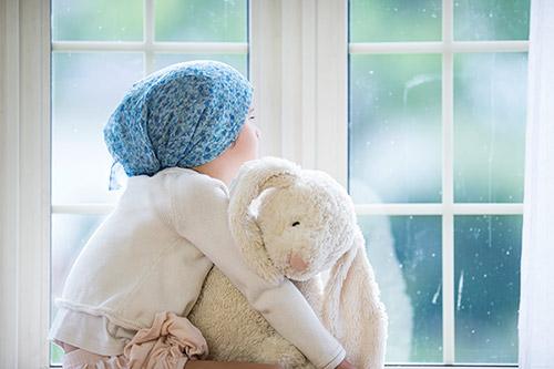 A young girl with cancer wearing a scarf over her head and holding a stuffed animal