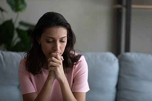 Worried young woman praying in her living room