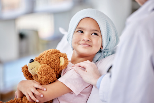Smiling little girl hugs her teddy bear while in the hospital for cancer treatment
