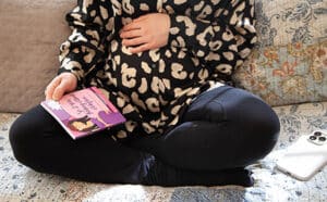 Pregnant woman seated cross-legged with her phone to her left and So I Was Thinking About Adoption to her right